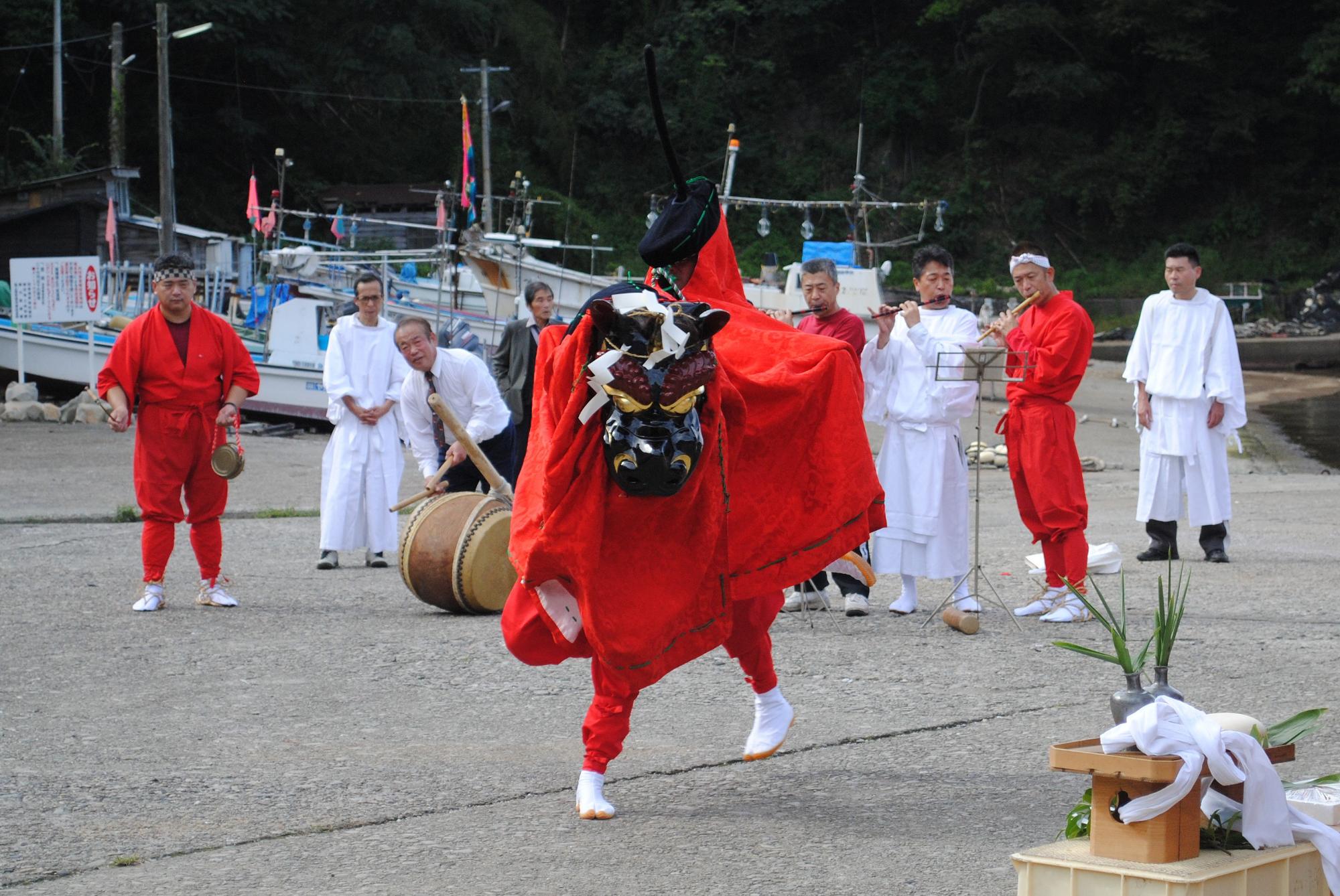 演奏する赤や白の和装をした人たちの前で赤い獅子舞が舞っている写真