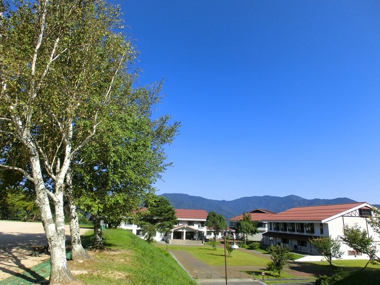 植林のある広場に赤い屋根をした建物がある写真