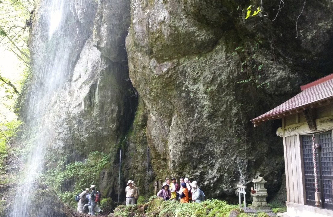 滝が落ちているゴツゴツした崖のそばを通る人たちの写真