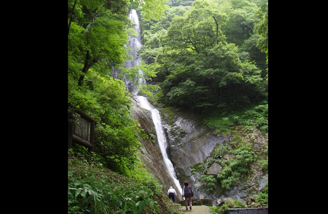 崖の上から流れてくる滝を眺める人の写真