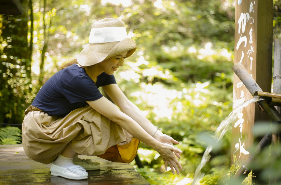 湧き水に両手を出す帽子をかぶった女性の写真