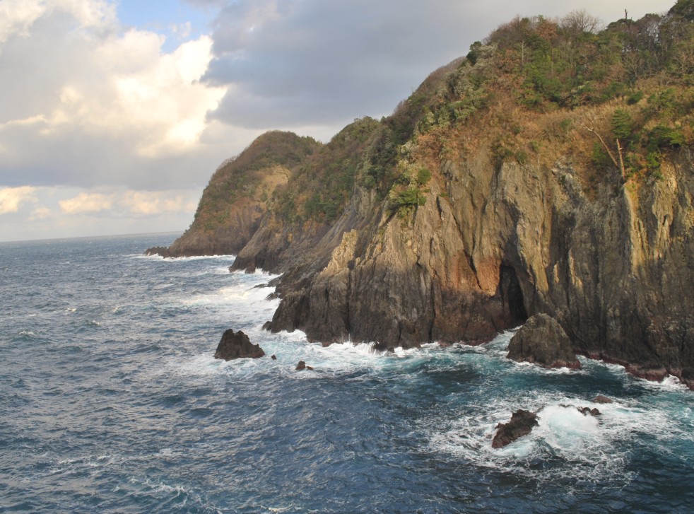 岩肌の見える島に波しぶきが上がっている写真