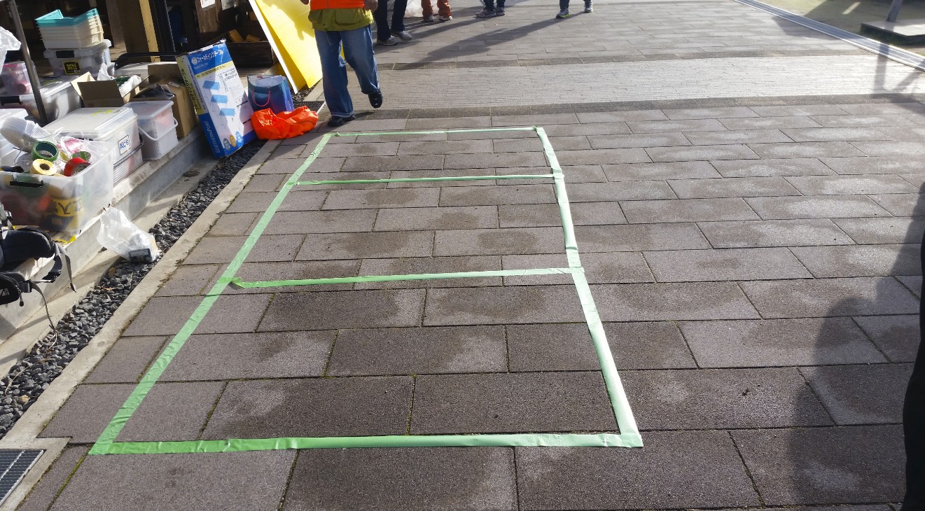 緑色のテープで3つの枠が作られた舗装路の写真