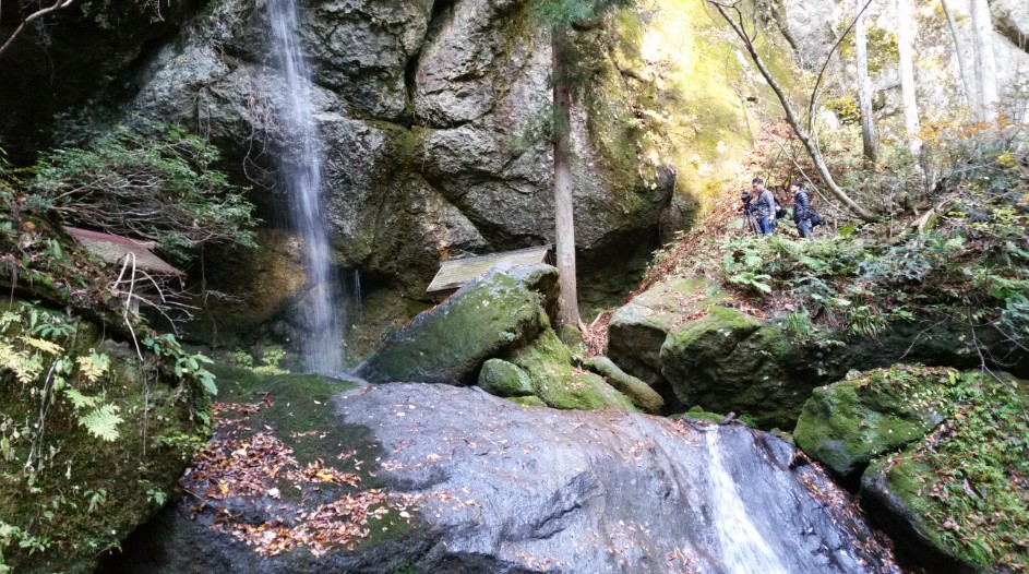 滝のそばの岩場に立っている2人の写真