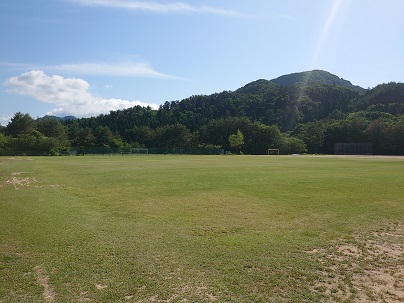青空の下遠方に小山が見える一面芝生のグラウンドの写真