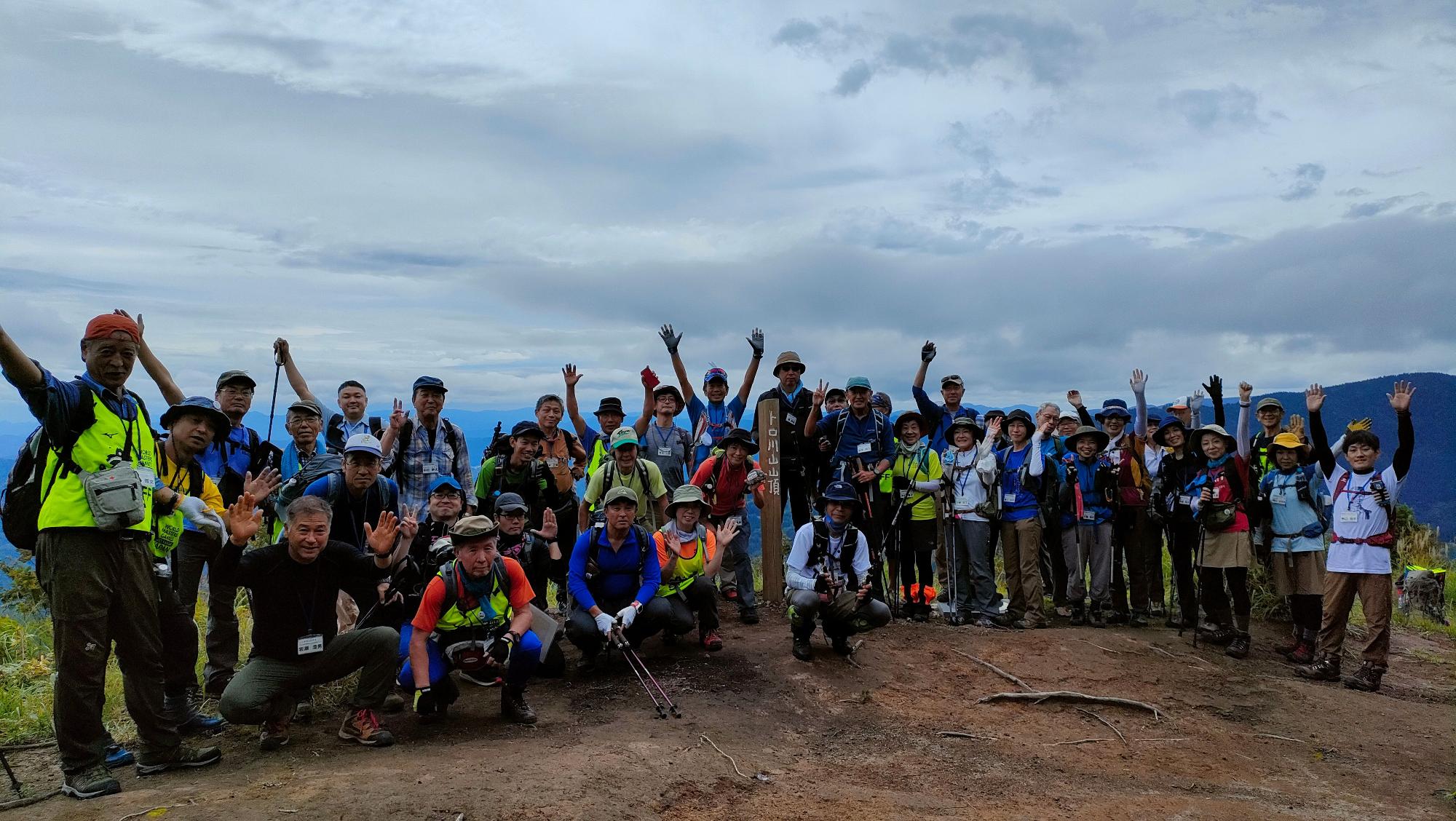 山頂で手を上にあげて喜んでいる登山客の集合写真