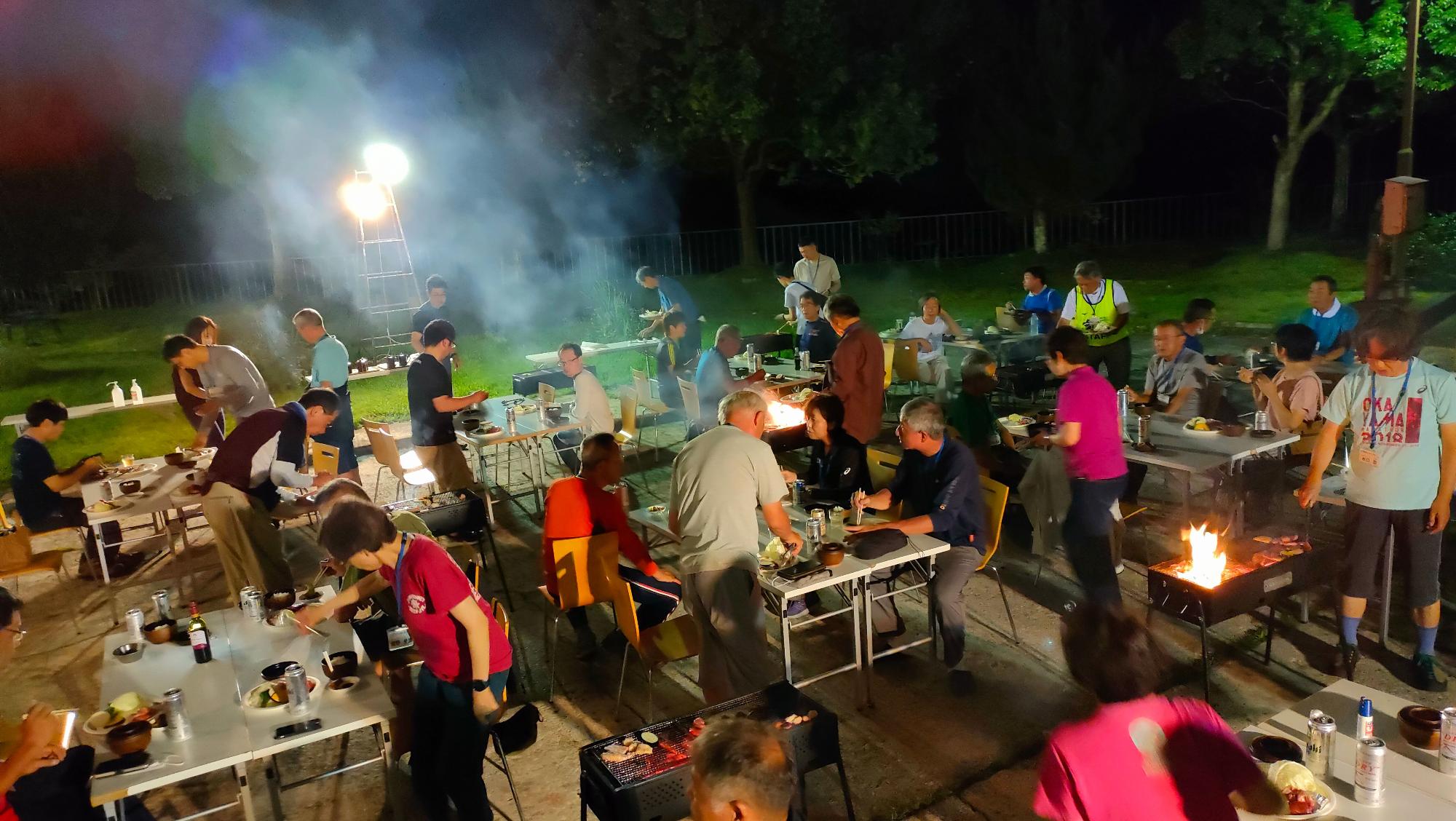 大勢の人たちが夜にバーベキューをしている写真