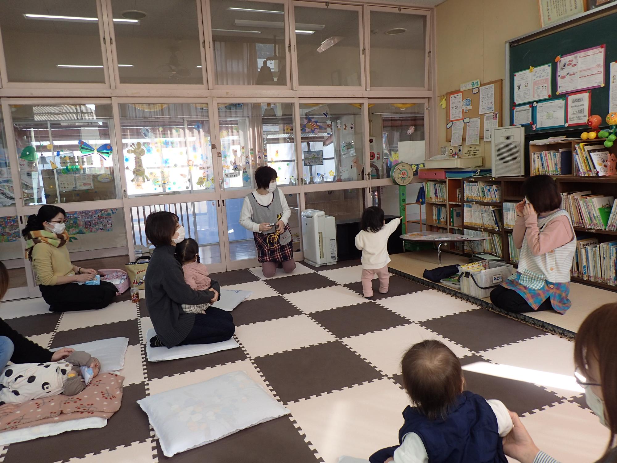 本棚を指さす子供を見つめる複数の親子と先生2名の写真