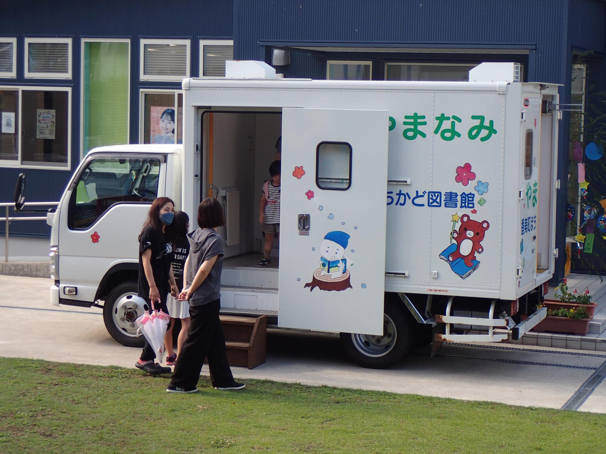 ドアの付いたトラックの荷台に入る子供と大人の写真