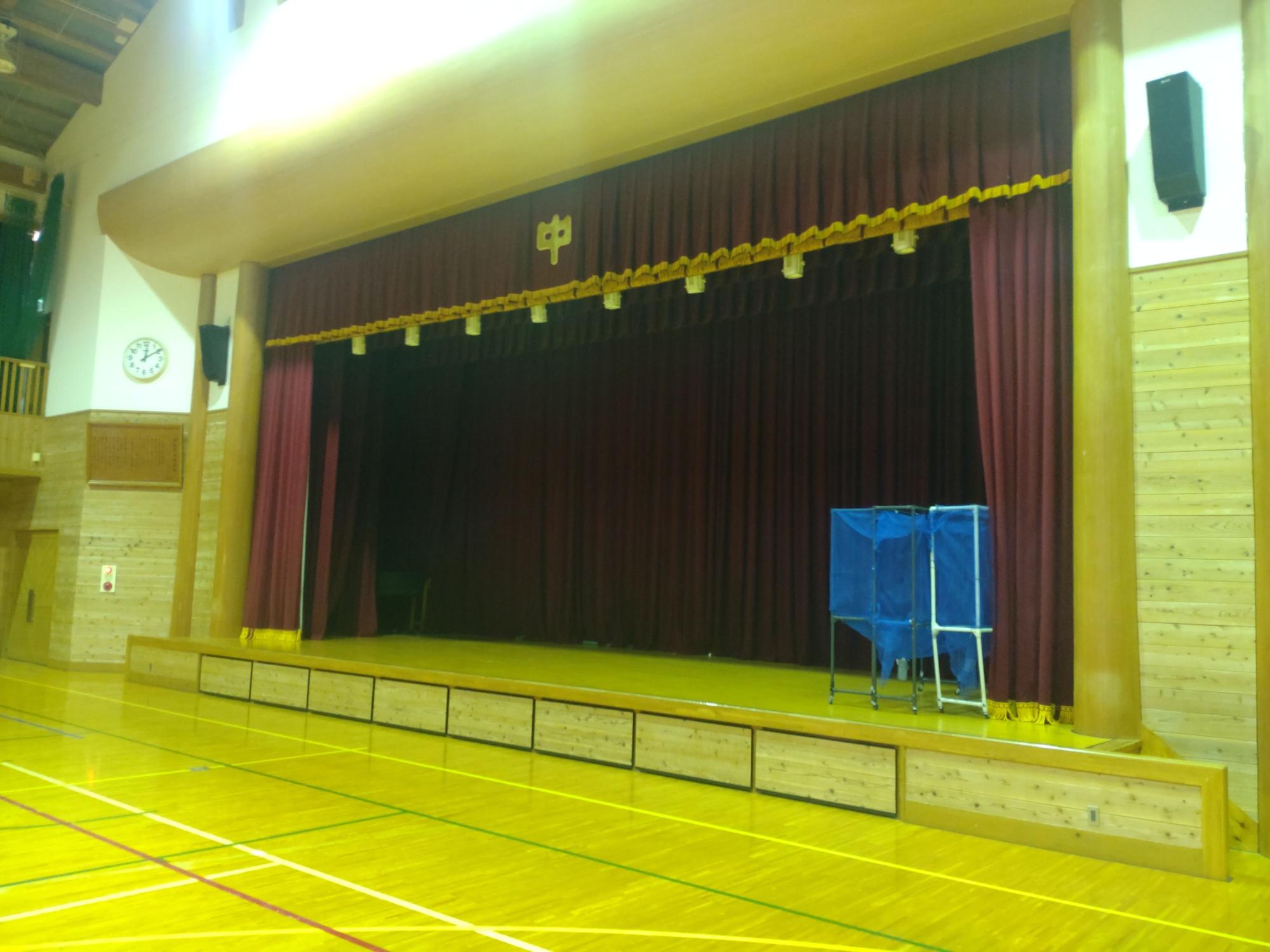 えんじ色の幕がセットされている体育館のステージの写真