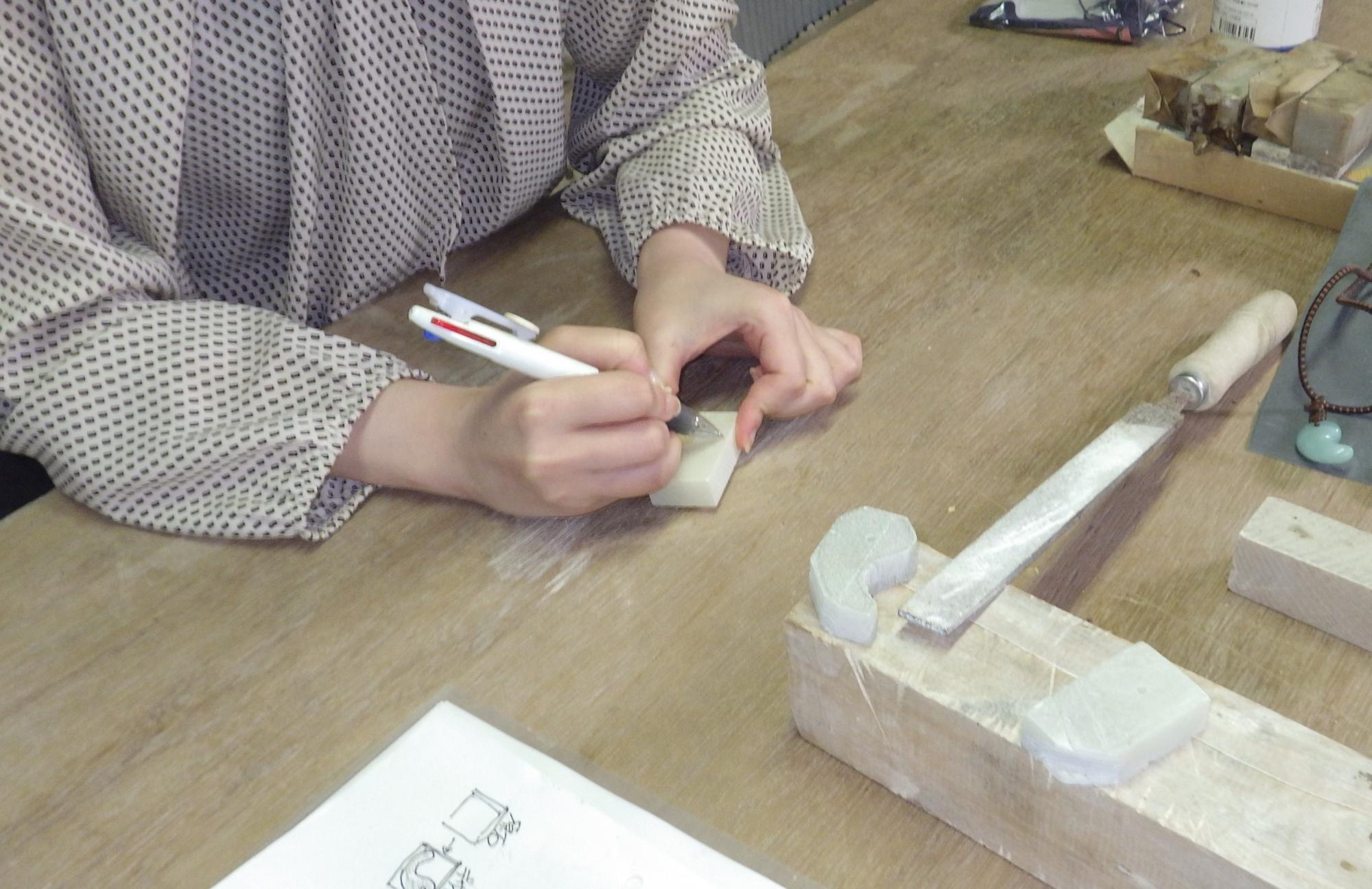 白い石にボールペンで線を描いている人の手元の写真