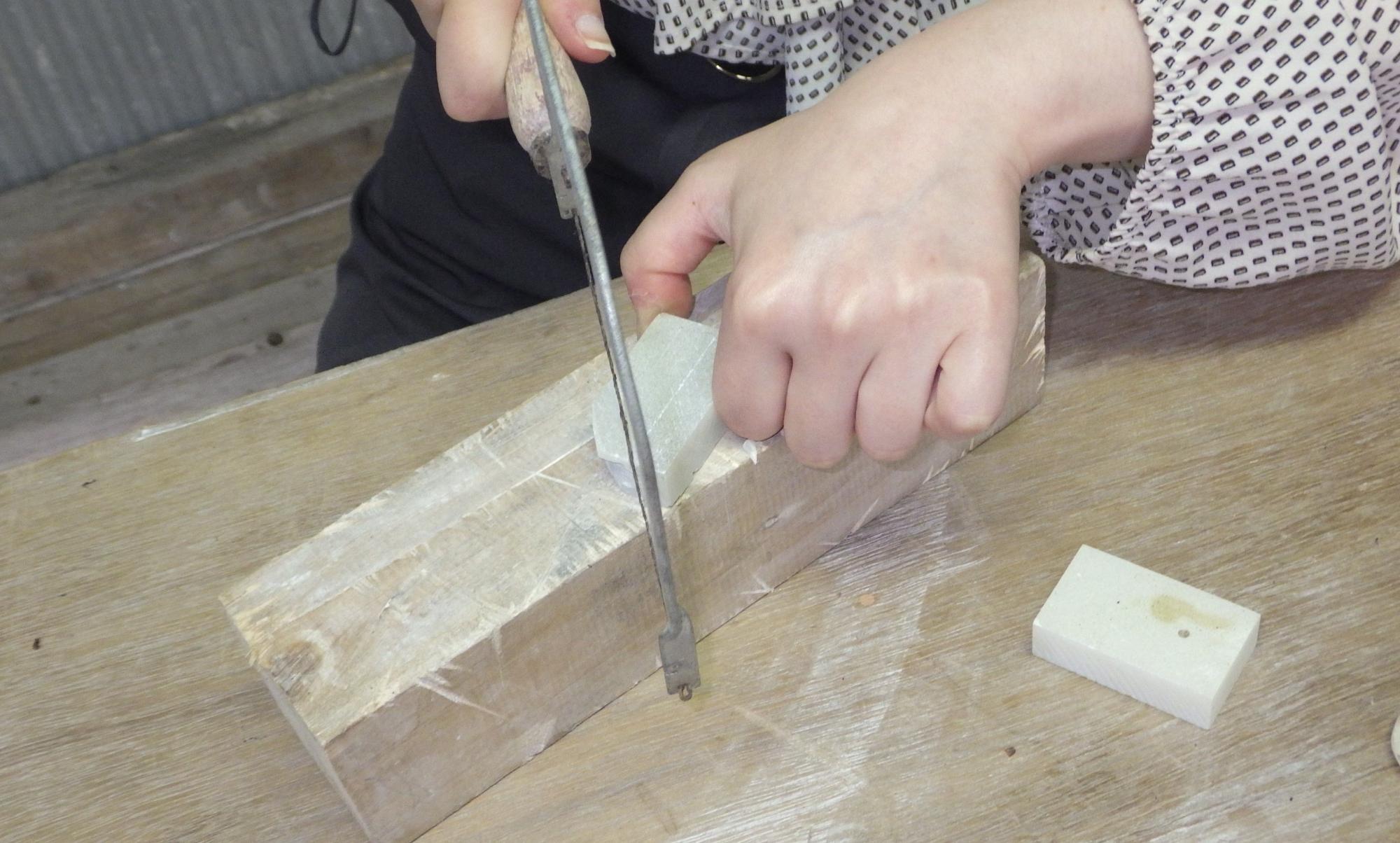白い石を糸ノコギリで切っている人の手元の写真