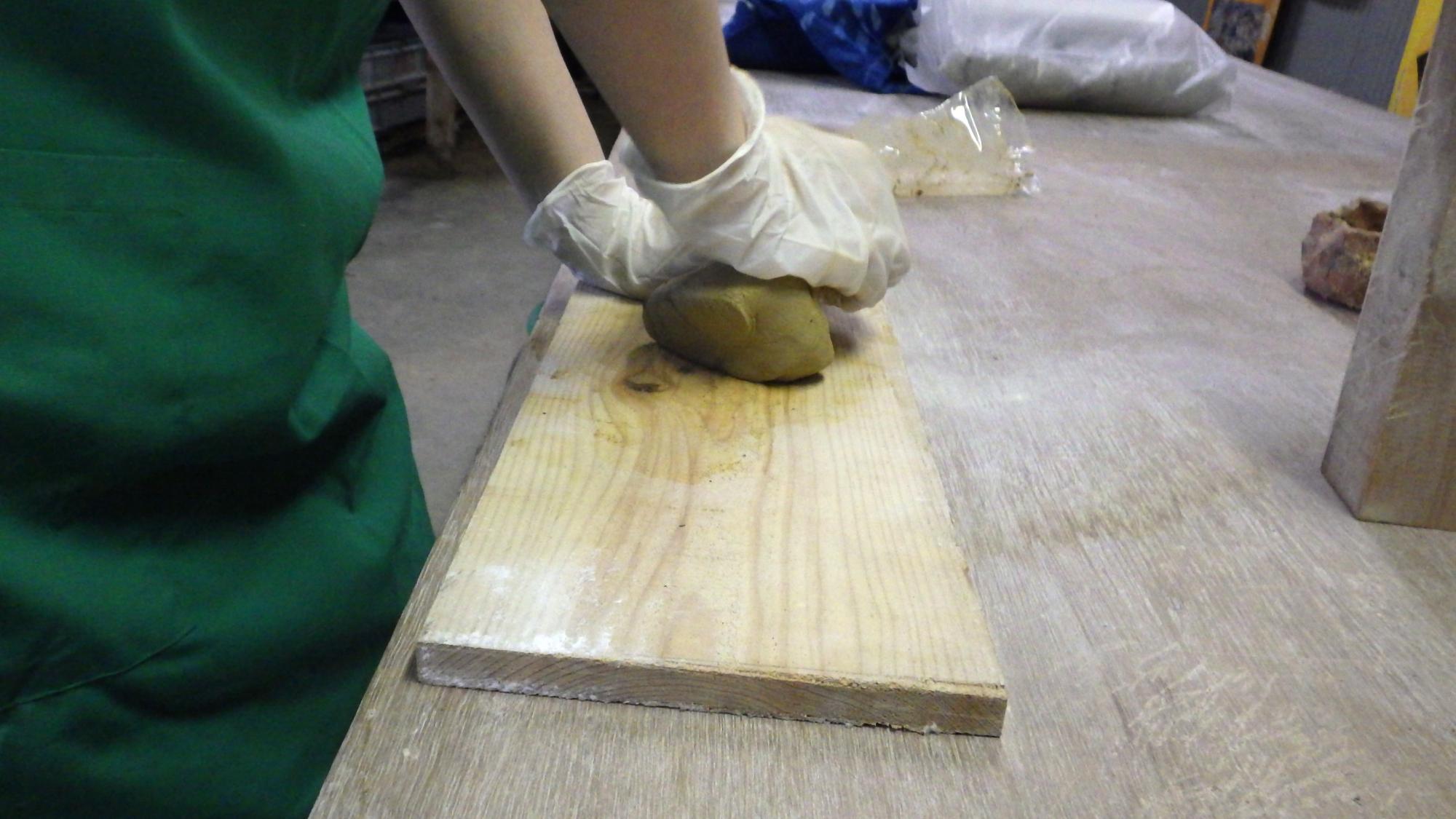 木の板の上で体重をかけながら粘土をこねる人の手元の写真