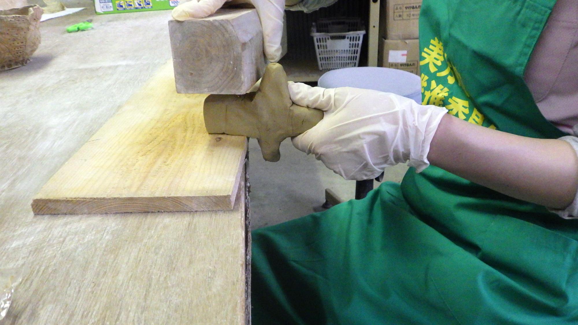 四角い木を粘土に当てている人の手元の写真