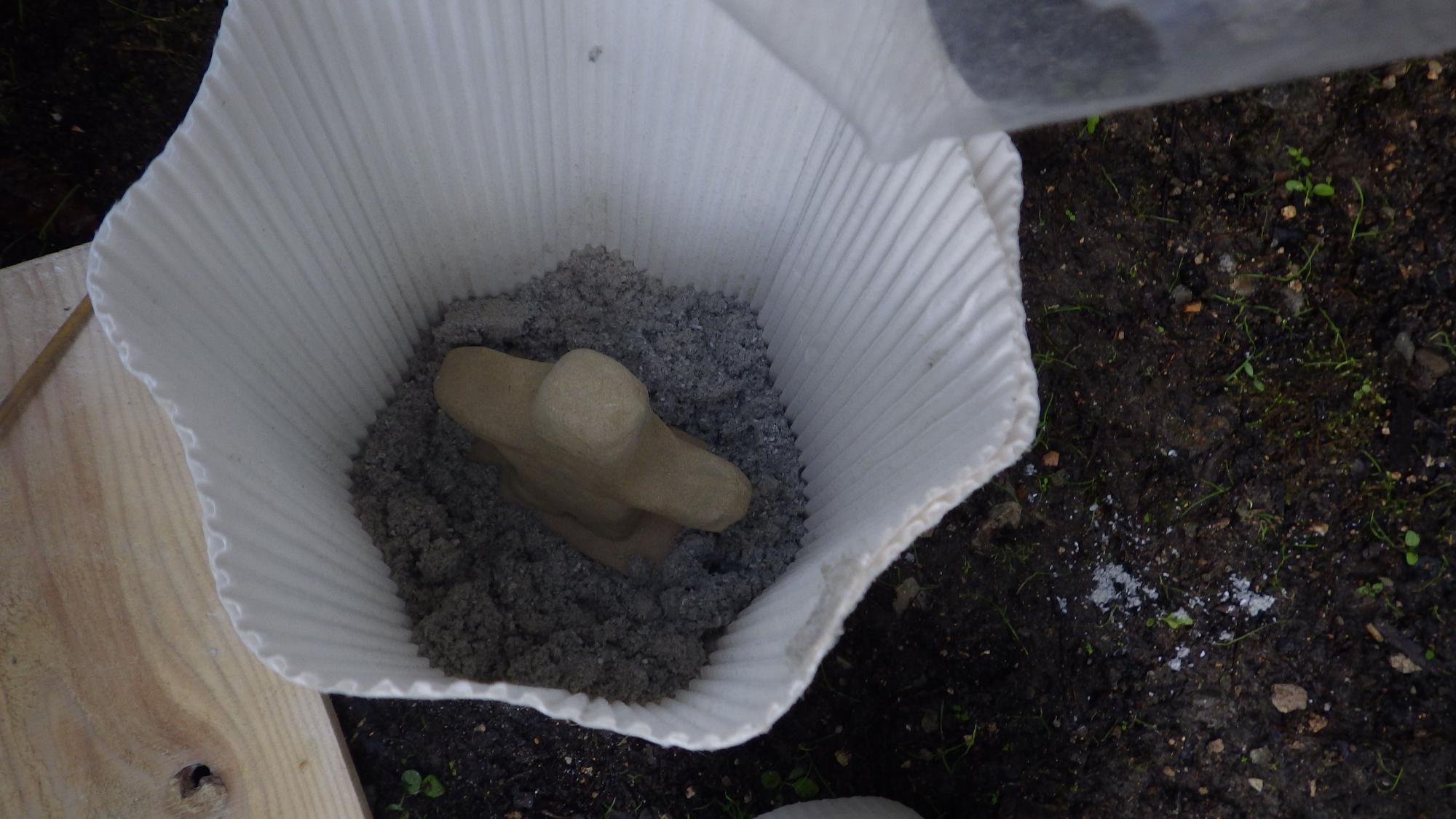 中に灰と粘土の置物が入った白い筒の写真