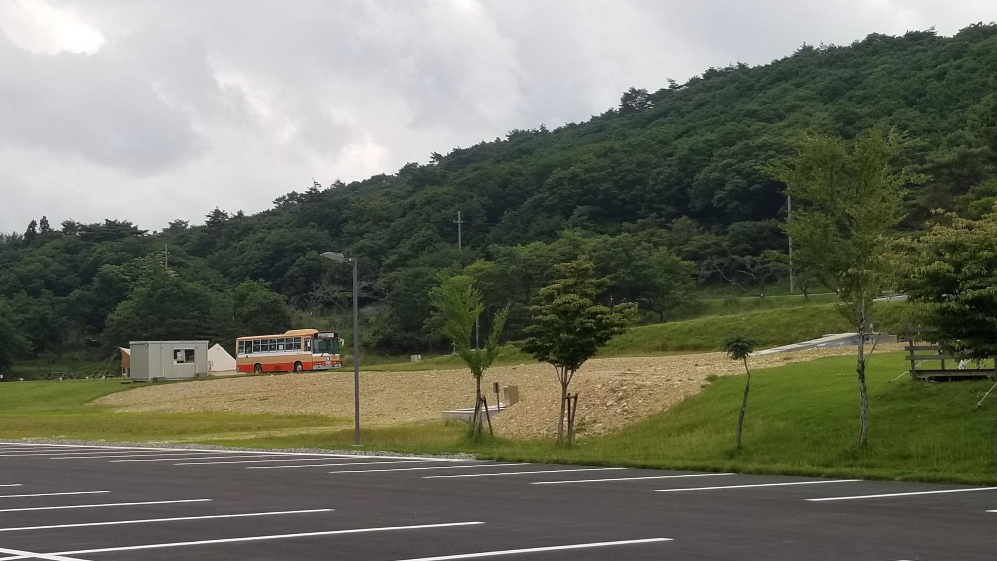 山の手前の道を走るバスとそのさらに手前にある駐車場の写真