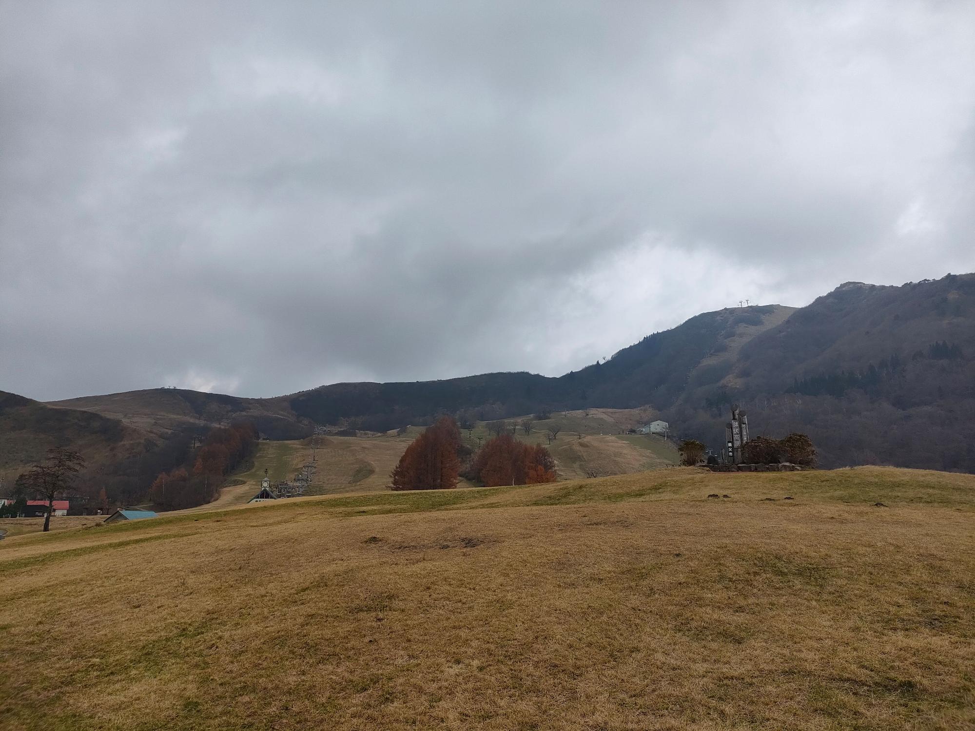 周りを山に囲まれた傾斜のある草原の写真