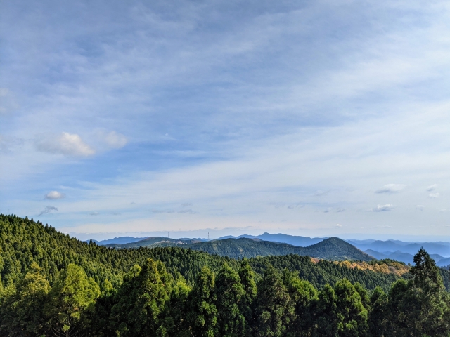 うっすら雲のかかった空の下に広がる山々の写真