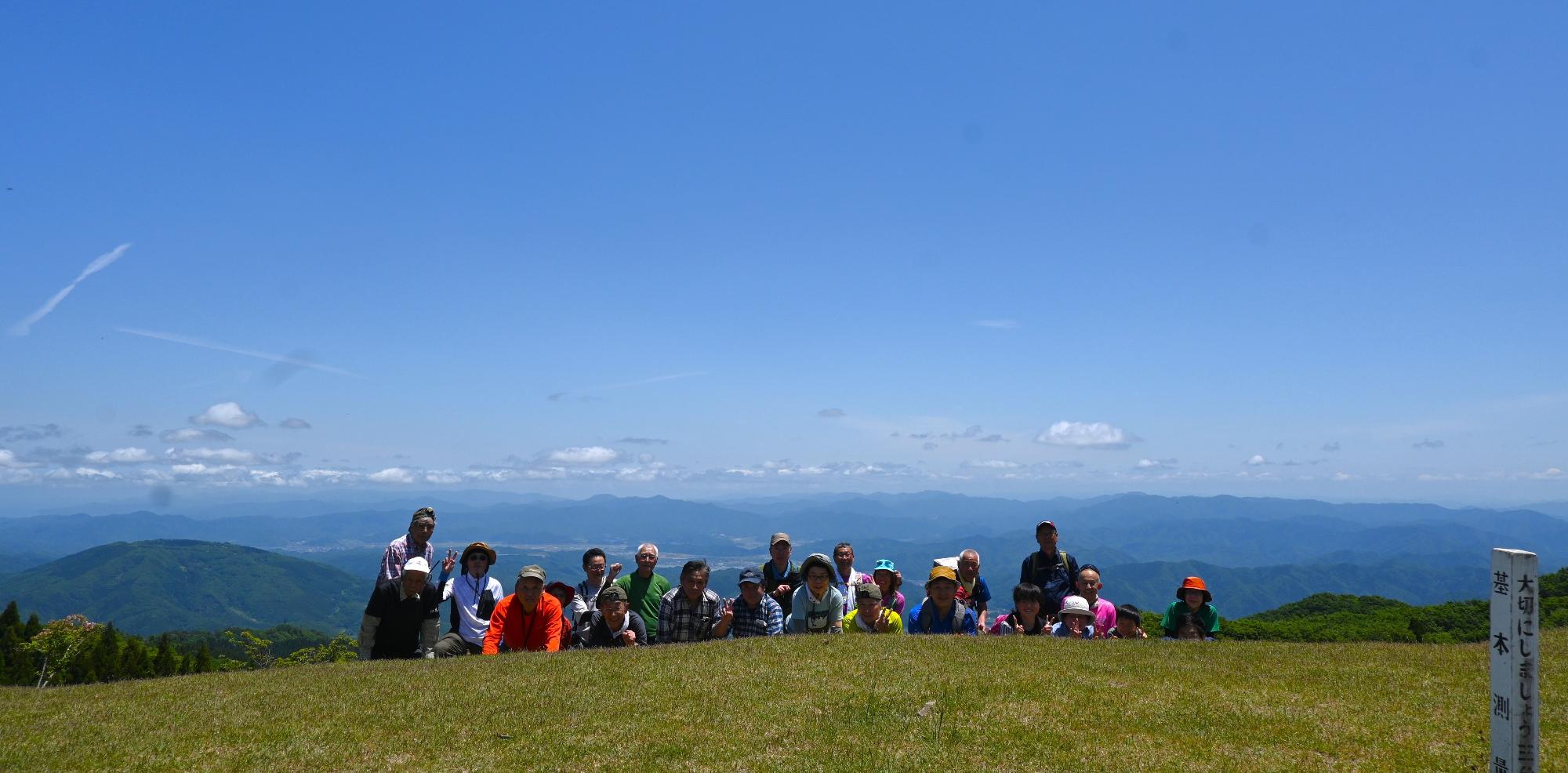 見晴らしの良い山頂で登山者が並んでいる写真