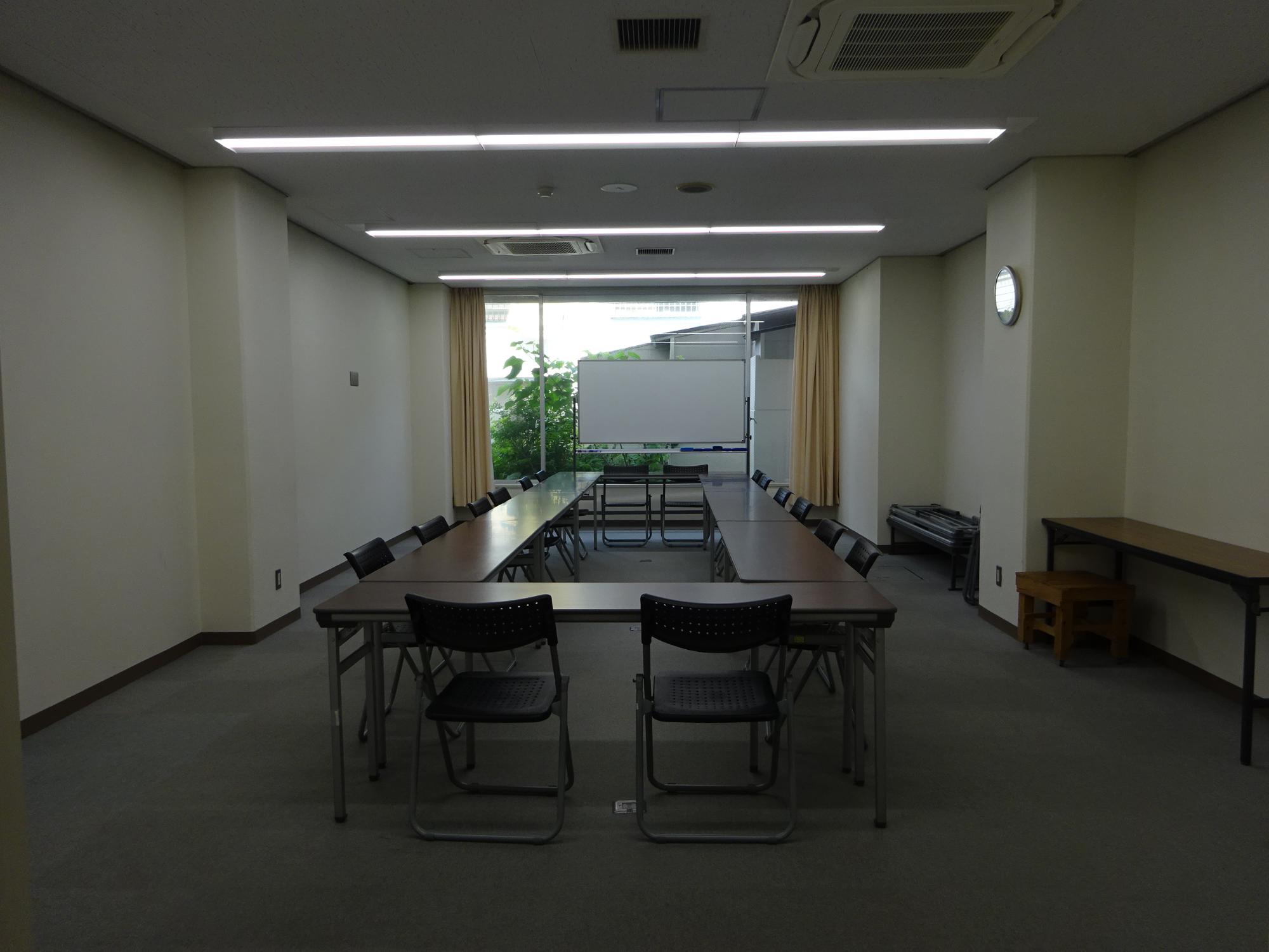 四角形に並んだ長机とホワイトボードの置かれた部屋の写真