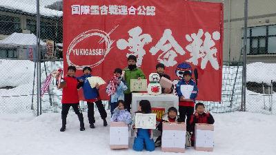 雪合戦と書かれた赤旗の前で景品と賞状を見せている子供たちの集合写真