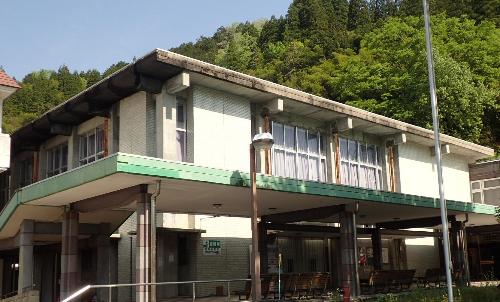 道路と山に挟まれた横長の大きな建物の写真