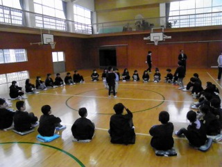 体育館で円になって集会を行う子どもたちの写真