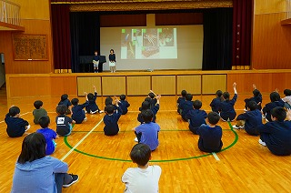 体育館で床に座り集会に参加する子どもたちの写真