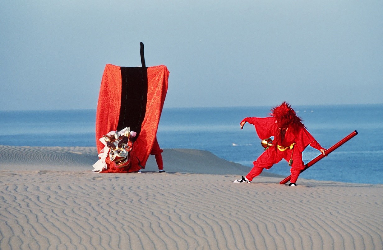 鳥取砂丘で舞を踊る赤い衣装を纏った人の写真