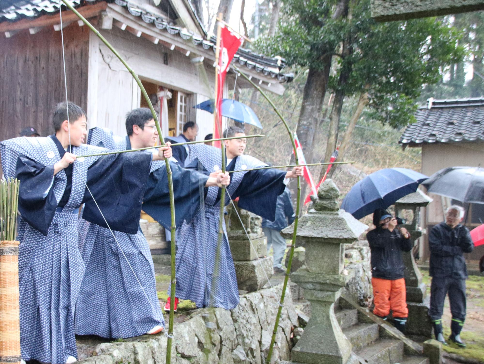崖上で行われている百手の儀式の写真。裃を着た3人が弓をかまえている。