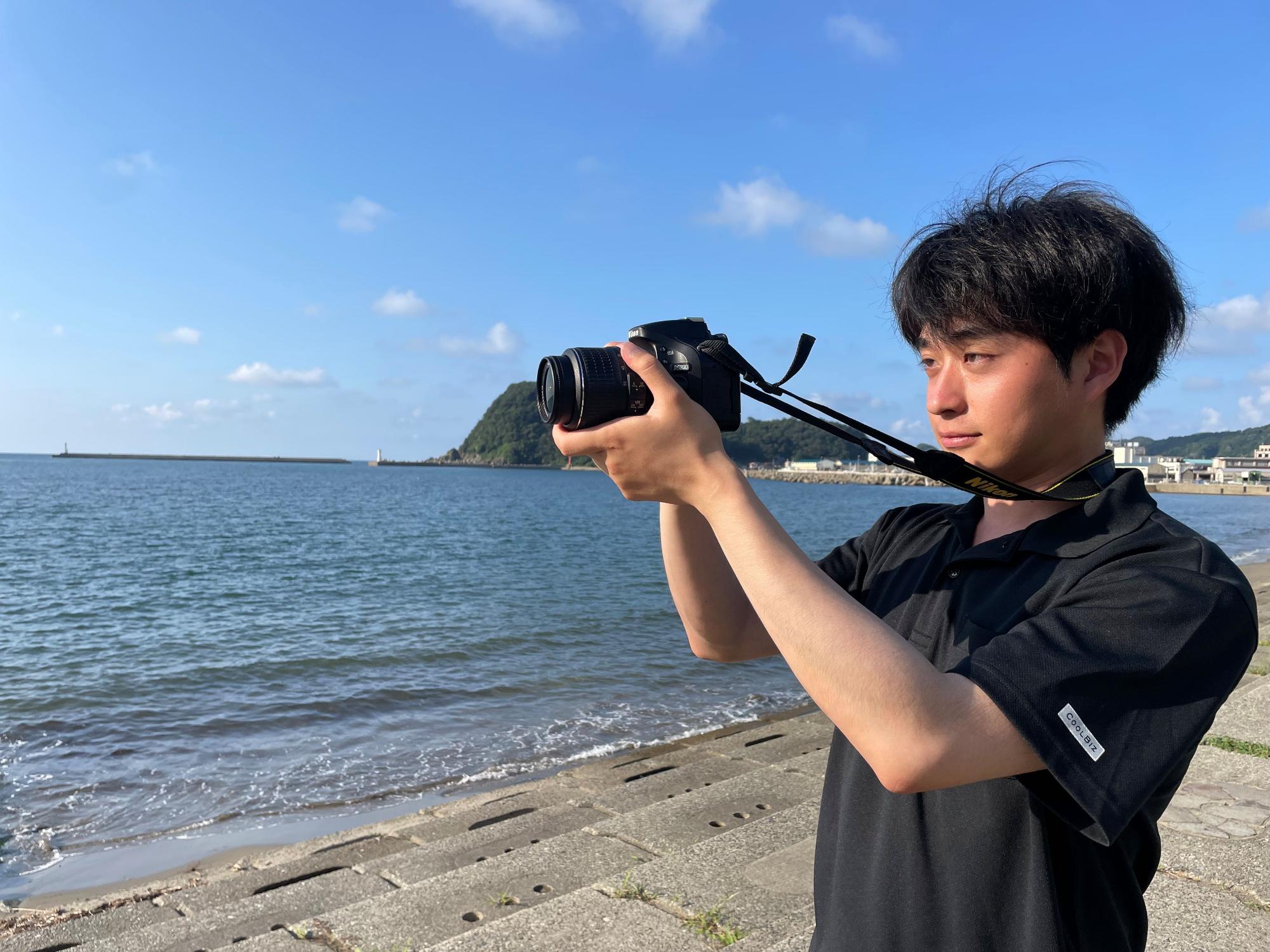 海辺でカメラを構えている高橋 昇吾さんの写真