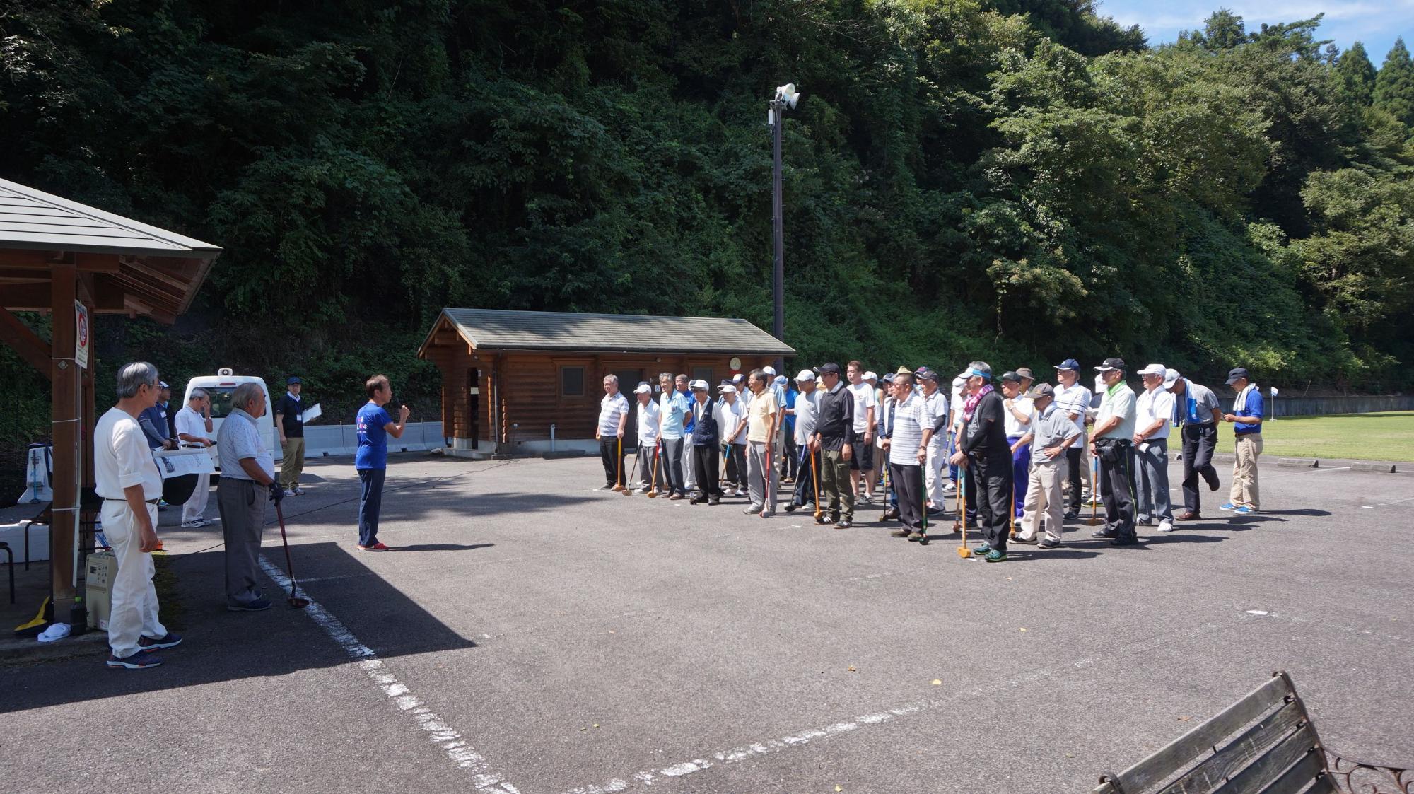 アスファルト路面の上で青い服の男性の説明を聞く参加者の写真