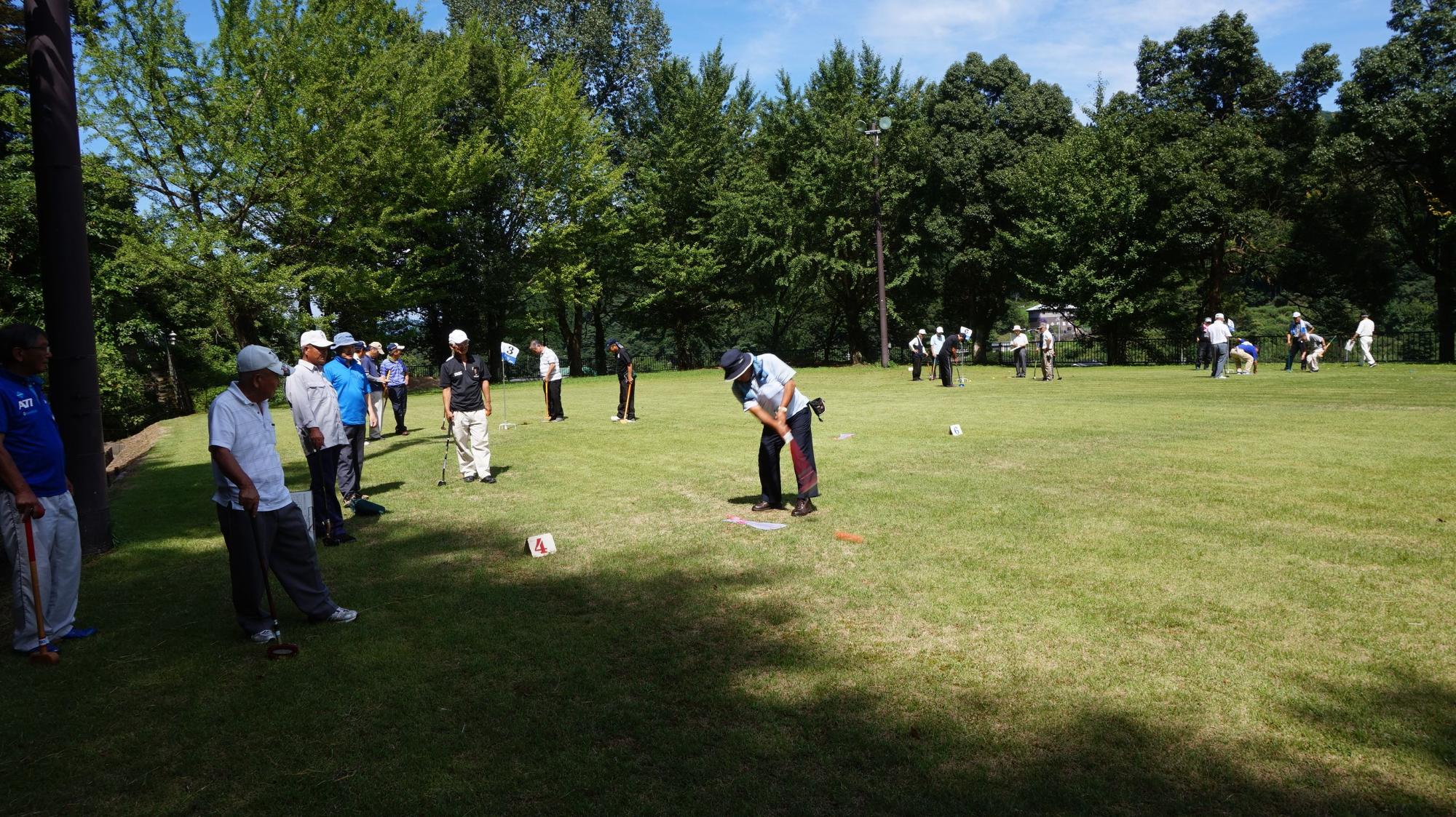 芝生の上で多くの参加者とともにゲートボールを楽しむ男性の写真