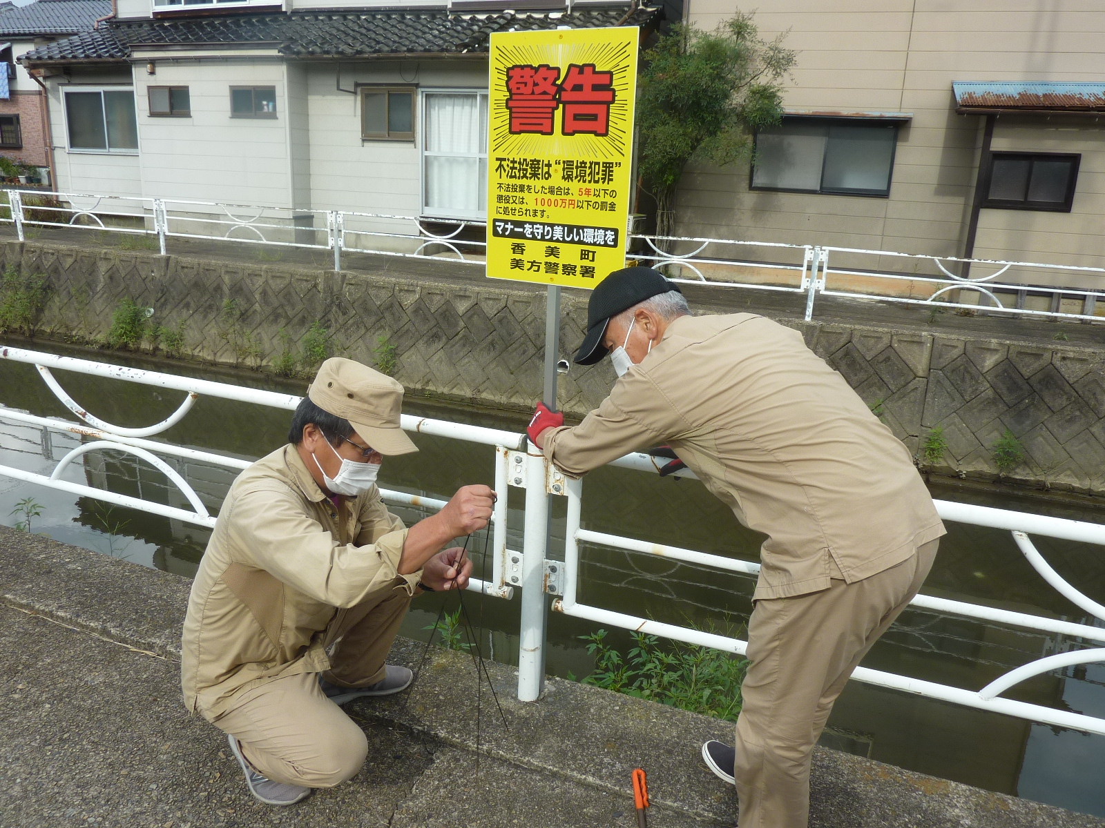 作業服姿の男性2人組が不法投棄禁止の警告看板を設置している写真