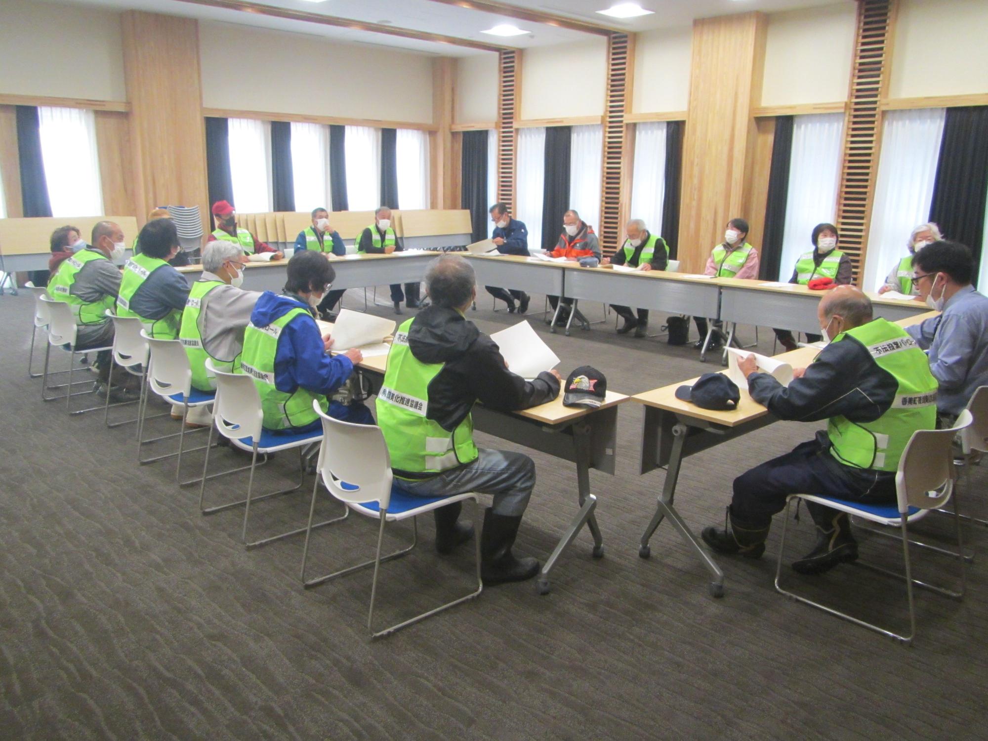 緑のチョッキを着た人々が会議室のテーブルを囲み会議をしている写真