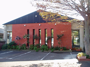 駐車場の奥にある赤い壁と青い三角屋根の建物の写真