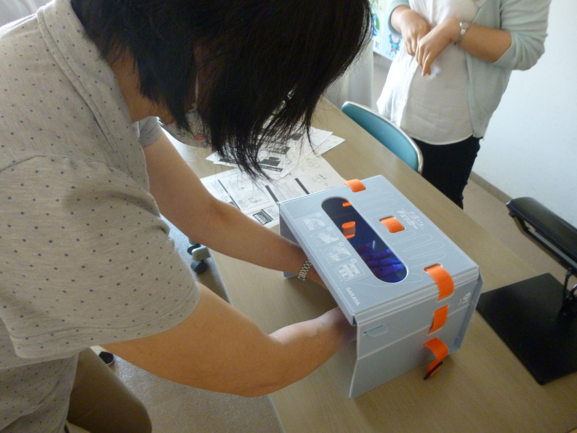 机に置かれた灰色の小型の機械に両手を入れている女性の写真