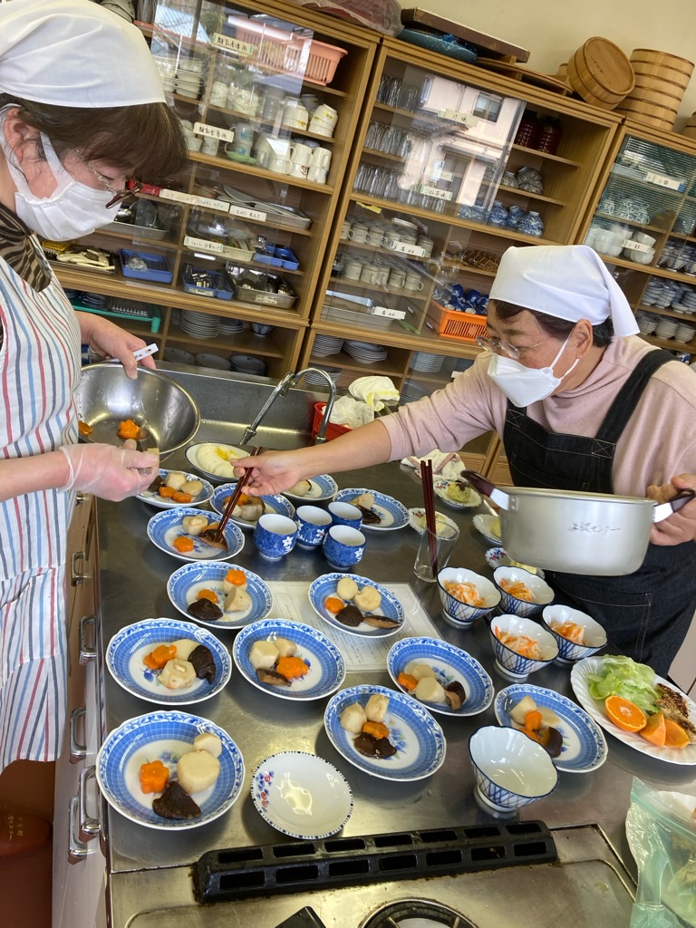 女性二人が料理をたくさんの皿に盛り分けている写真