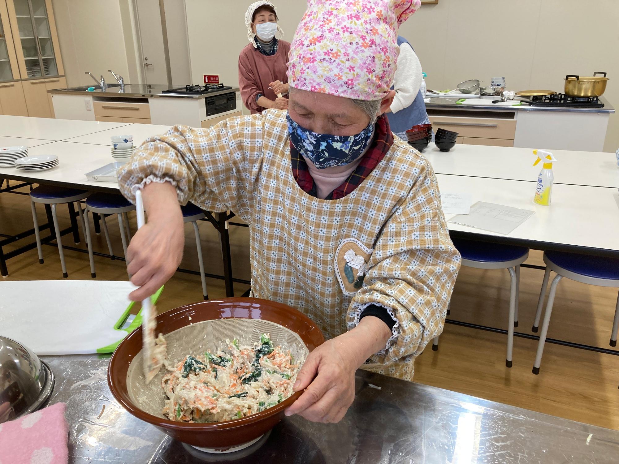 三角巾を頭に付けた女性がすり鉢の中をかき混ぜている写真