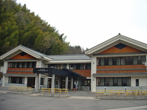 木が生い茂る手前に建つ三角屋根の建物の外観の写真